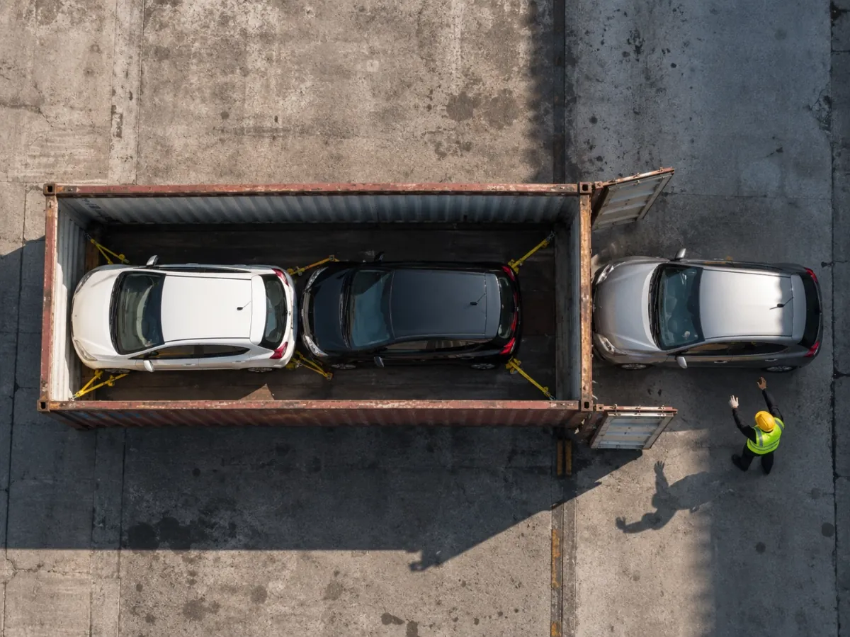 Overhead view of three cars secured inside an open shipping container at a port facility, ready for overseas transport.